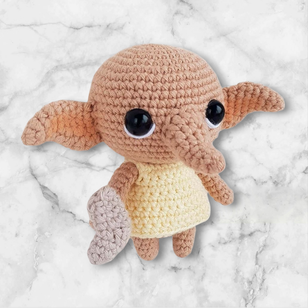 Crocheted creature with a round body and large eyes on a marble background