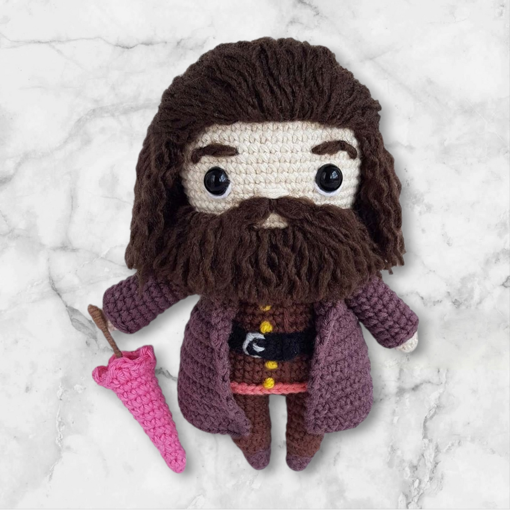 Crocheted doll resembling a character with a beard and coat, holding a pink object on a marble background