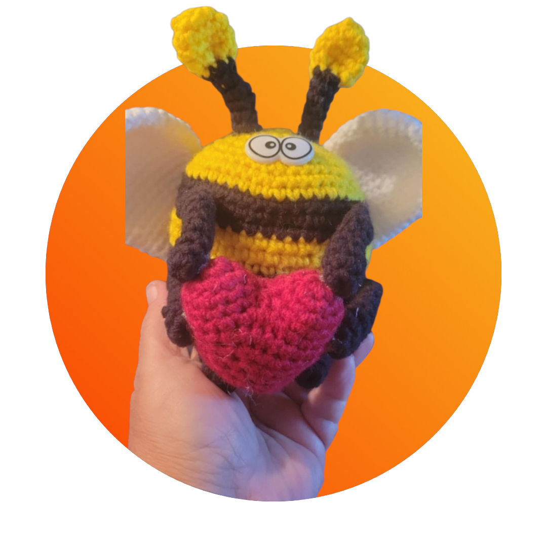 Hand holding a colorful crochet bee toy against an orange background